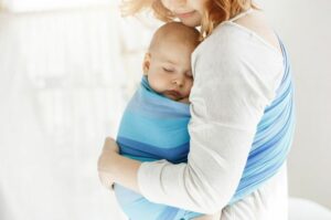 Photo d'une maman portant son bébé dans une écharpe illustrant l'article des différents types de portage pour un bébé